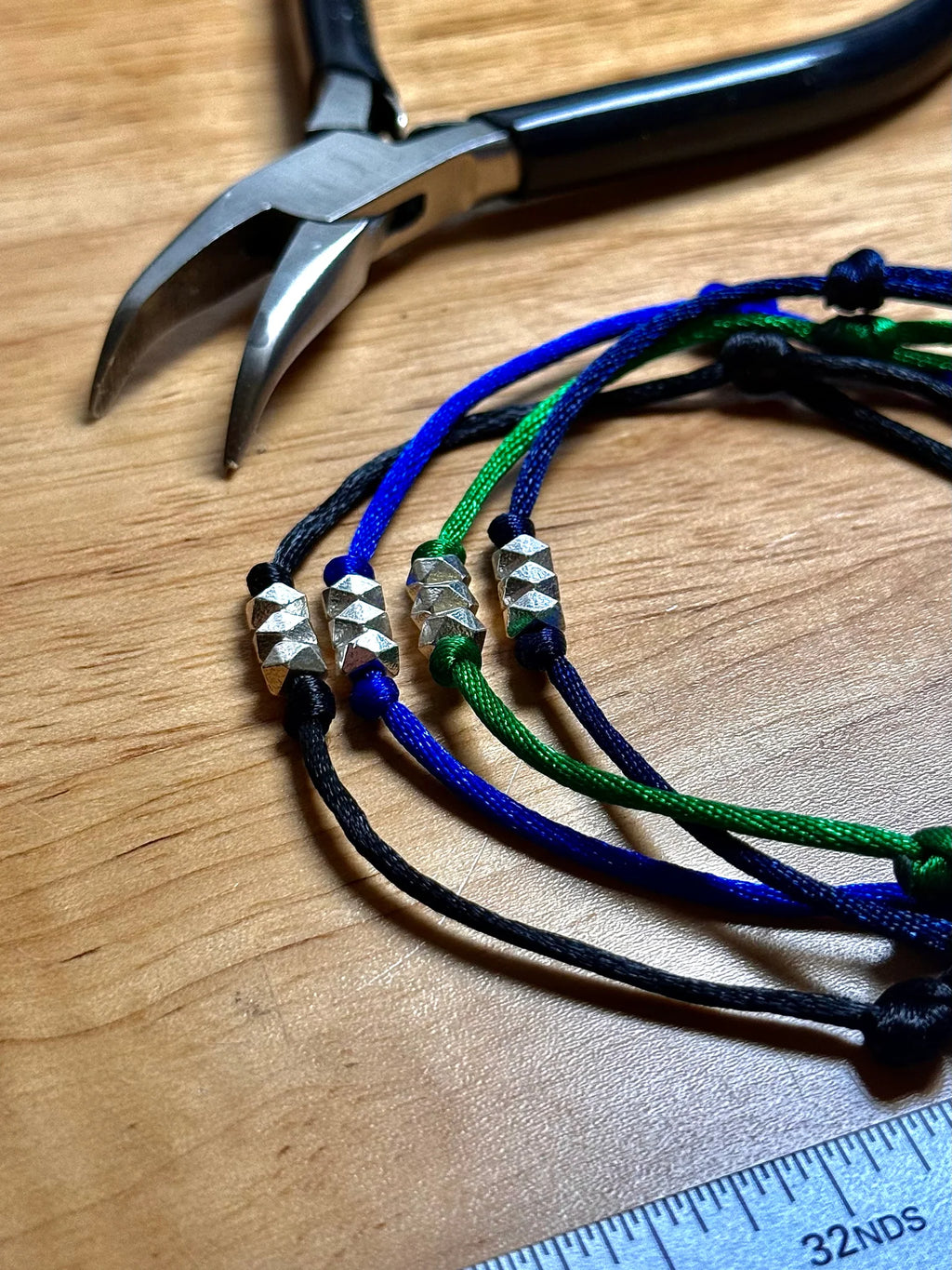 Four colorful bracelets with silver beads on a wooden surface with pliers and a ruler.